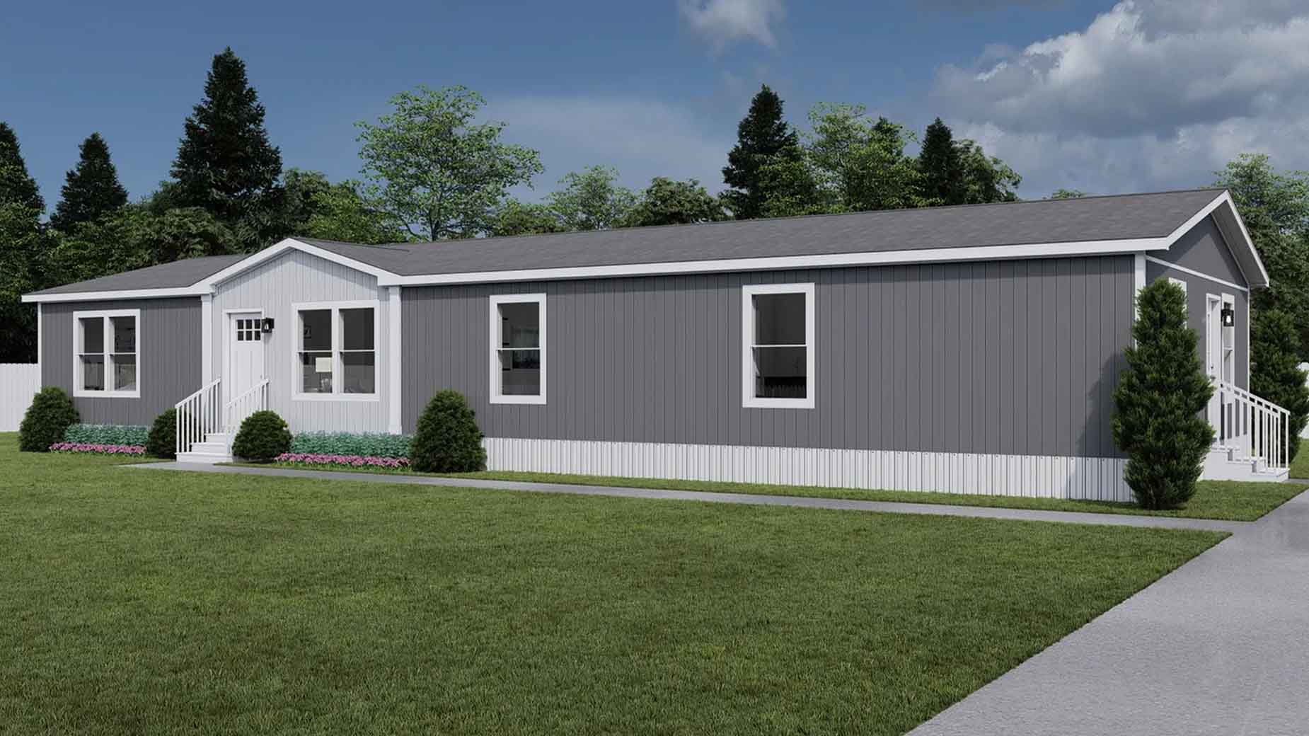A gray and white manufactured home with steps sits surrounded by grass, bushes, and trees under a cloudy sky.