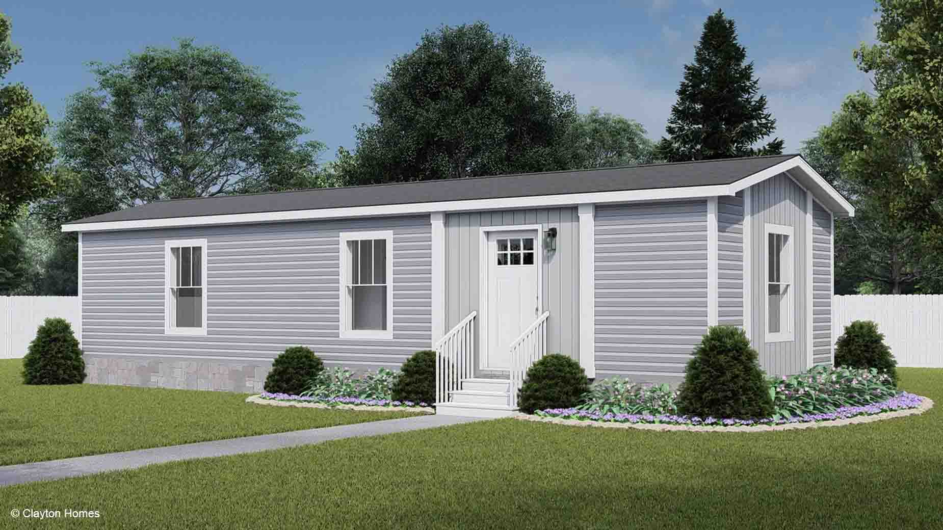 A small gray manufactured home with white trim, a front door, steps, and shrubs in the yard offers cozy living in a charming setting.
