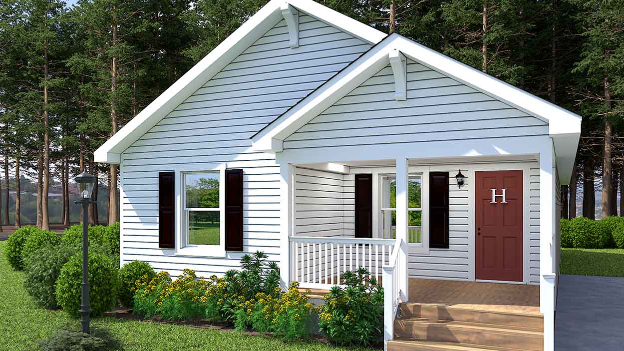 Charming small white modular home with a front porch, brown door, flowers, and green lawn, surrounded by trees.